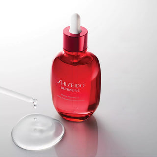 Shiseido Ultimune Power-protecting Serum in a translucent red glass dropper bottle, shown with a glass pipette and a clear droplet on a light gray reflective surface.