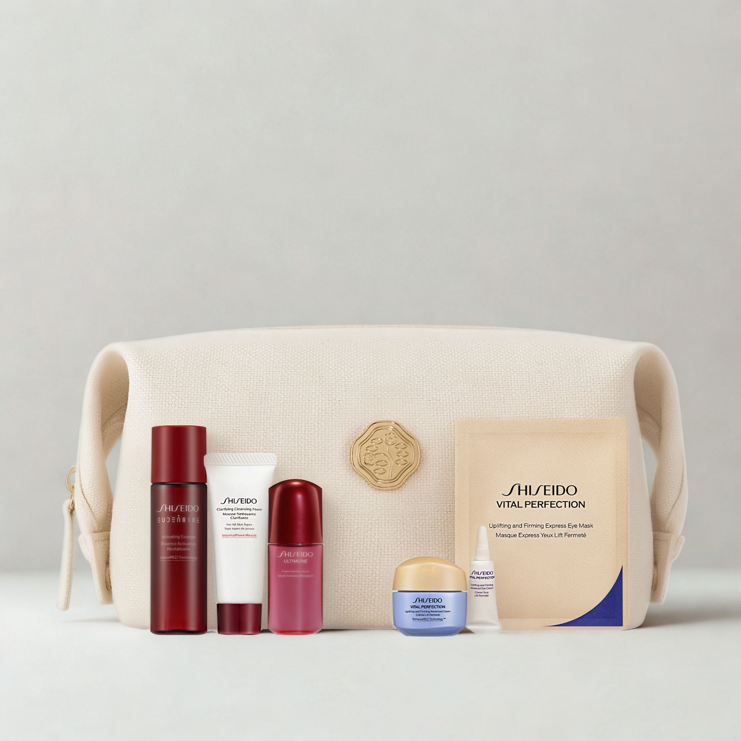 A Shiseido gift set arranged in front of a cream-colored canvas pouch. The set includes a Shiseido Ultra Pro Red Cell Serum bottle, a white tube, a pink/red cap bottle, a blue and gold cream jar, a small white tube, and a beige sheet mask packet, all set against a neutral light gray background.
